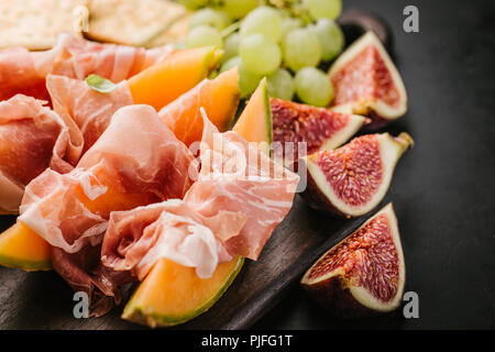 Spagnolo gustosi cibi tradizionali - antipasti mediterranea con Melone e prosciutto a bordo su sfondo scuro. Primo piano. Orizzontale con copia spazio. Foto Stock