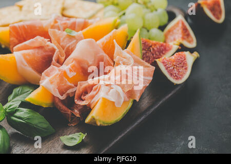 Spagnolo gustosi cibi tradizionali - antipasti mediterranea con Melone e prosciutto a bordo su sfondo scuro. Primo piano. Orizzontale con copia spazio. Foto Stock