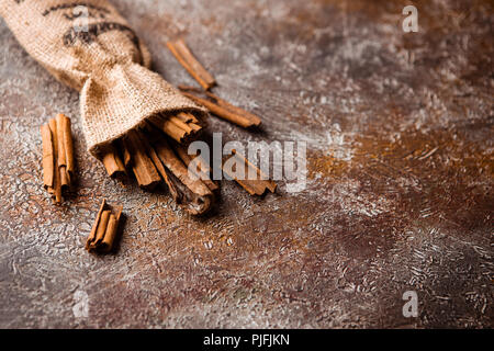 Bastoncini di cannella in una borsa di tela su grunge backround marrone Foto Stock
