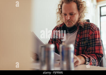 L'uomo la lettura di alcuni documenti in ufficio. L uomo è casuals seduti al tablet e passando attraverso i documenti aziendali. Foto Stock