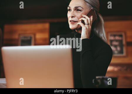 Ritratto di senior bella donna seduta al coffee shop e parlando al cellulare. Imprenditrice rendendo chiamata mentre è seduto presso il cafe. Foto Stock