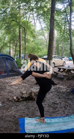 Giovane donna andando fino in Thiruvikramasana / Split permanente yoga pongono in campeggio nella foresta Foto Stock