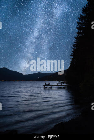 Due persone sedute sul dock con cielo stellato via lattea Foto Stock