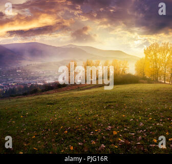 Nuvoloso Tramonto in montagna. splendida campagna in autunno. alberi con foglie di colore giallo sulla collina e la nebbia giù nella valle Foto Stock