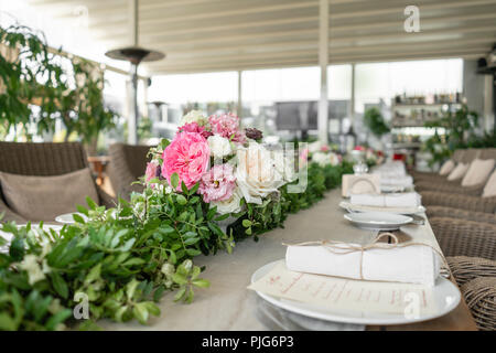 Ordinatamente intrecciati in un tubo sala da pranzo igienico decorate con un rametto di pistacchio. Banchetti per matrimoni o cene di gala. Il tavolo e sedie per gli ospiti, Servita con posateria e stoviglie. party sulla terrazza Foto Stock