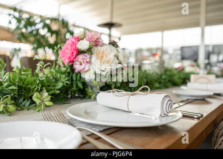 Ordinatamente intrecciati in un tubo sala da pranzo igienico decorate con un rametto di pistacchio. Banchetti per matrimoni o cene di gala. Il tavolo e sedie per gli ospiti, Servita con posateria e stoviglie. party sulla terrazza Foto Stock