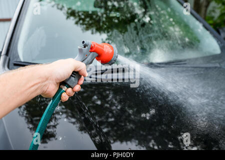 Uomo che pulisce la sua auto in self service carwash, spazzola lasciando tratti di shampoo sul faro anteriore.il lavaggio di automobile manuale auto lavaggio self service station.lavaggio auto concept Foto Stock