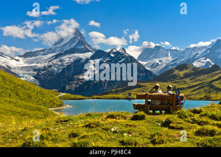 Gli escursionisti mettendo in pausa su una panca di legno al lago Bachalpsee, dietro i vertici Schreckhorn e Finsteraarhorn, Grindelwald Foto Stock
