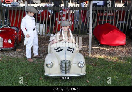 Joe Bain, 7, da Liverpool guarda come sua sorella Winnie, 10, conduce fuori del paddock nel suo Austin J40 automobile del pedale del giorno uno di Goodwood al Goodwood circuito motore a Chichester. Foto Stock