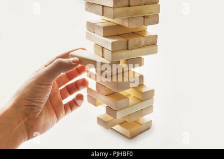 La torre da blocchi di legno e di mano d'uomo prendere un blocco. Il gioco dei dadi su sfondo bianco. Foto Stock