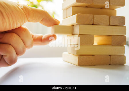 La torre da blocchi di legno e di mano d'uomo prendere un blocco. Il gioco dei dadi di close-up. Foto Stock