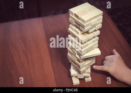 La torre da blocchi di legno e di mano d'uomo prendere un blocco. Il gioco dei dadi su un tavolo di legno. La vista dall'alto Foto Stock