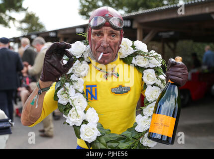 Un appassionato di Revival vestito come un pilota da corsa, in posa per una fotografia sul motore di un 1965 Lola-Chevrolet T70 Spyder del giorno uno di Goodwood al Goodwood circuito motore a Chichester. Foto Stock