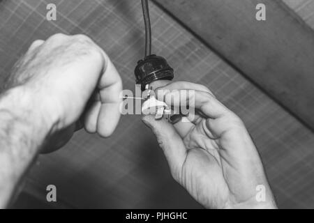 L'uomo elettricista installa una lampada elettrica titolare, foto in bianco e nero Foto Stock