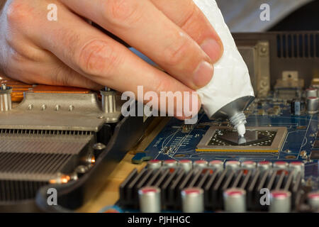 La riparazione di un computer. gli uomini le dita schiacciato da un tubo di pasta termica per il processore video. close-up di messa a fuoco selettiva Foto Stock
