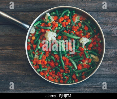 Cibo asiatico piatto. mix di vegetali di carote, piselli, fagioli verdi e cavolfiore in padella su un vecchio tavolo di legno, close-up vista da sopra. ph oscurata Foto Stock