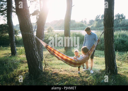 Giovane famiglia simpatico - mamma, papà e figlio di riposo nella natura, seduta in una amaca Foto Stock