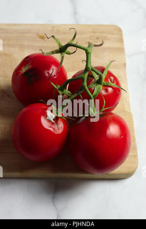 Pomodori marci con stampo sul tagliere di legno e marmo bianco superficie Foto Stock