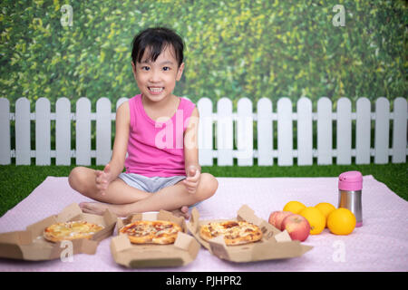 Cinese asiatici bambina di mangiare pizza al giardino esterno Foto Stock