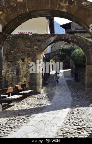 Un tranquillo percorso/road a Potes, Cantabria, Spagna settentrionale. Mostra una serie di tre archi e un ersone walking away fro la fotocamera. Foto Stock