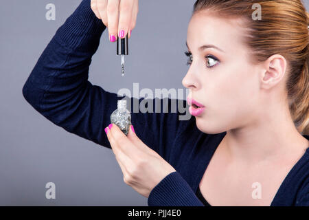 Ritratto di una giovane donna in possesso di un smalto per unghie con un aria di sorpresa Foto Stock