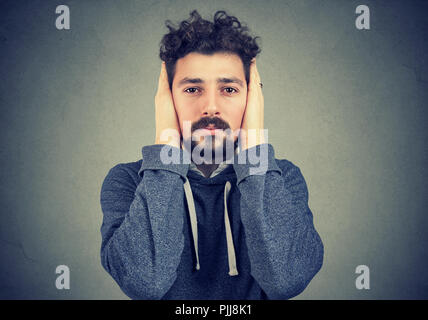 Giovane uomo che copre le orecchie evitando il rumore su sfondo grigio Foto Stock