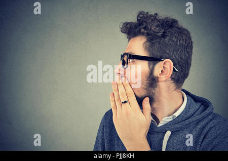 Giovane uomo che copre la bocca mentre spettegolare e raccontare segreti in sussurro. Foto Stock