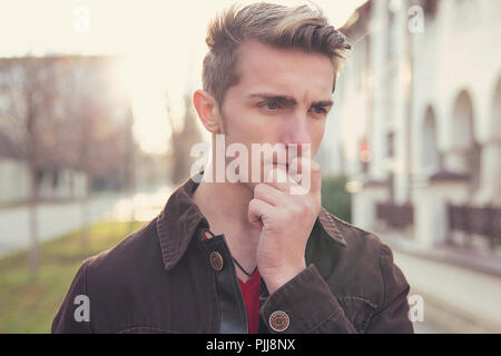 Giovane uomo preoccupato in dubbi di mordere le unghie e guardando lontano mentre permanente sulla strada Foto Stock