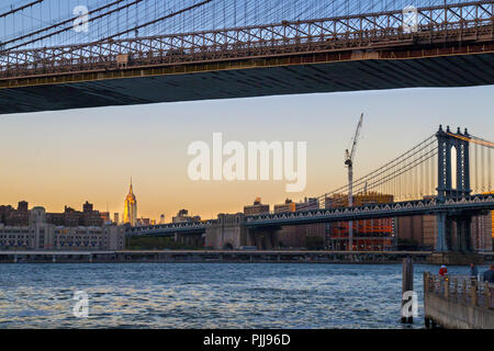 New York City ponti, Manhattan Bridge visualizza e ponte di Brooklyn davanti, Empire State Building in distanza, la luce del tramonto, NY USA Foto Stock