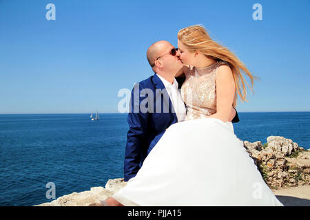 Nozze. Coppia felice giorno matrimonio. Bella Sposa e lo sposo in spiaggia. Allegro coppia sposata baciare e seduti in riva al mare. Coppie in viaggio di nozze. Foto Stock