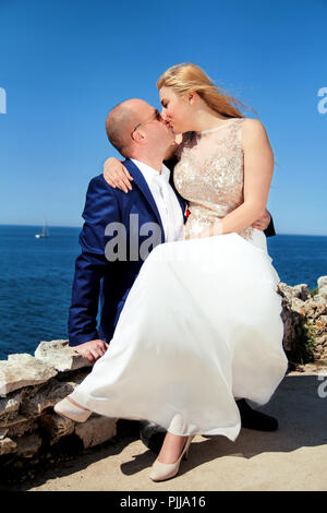 Nozze. Coppia felice giorno matrimonio. Bella Sposa e lo sposo in spiaggia. Allegro coppia sposata baciare e seduti in riva al mare. Coppie in viaggio di nozze. Foto Stock