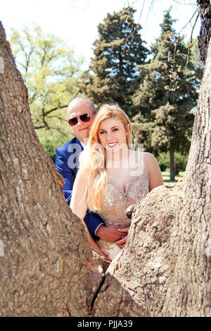 Nozze. Happy sposi nella foresta. Bella Sposa e lo sposo. Una coppia felice di stare dietro a un grande albero di alberi. Un matrimonio giovane. Foto Stock