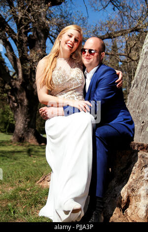 Nozze. Happy sposi nella foresta. Bella Sposa e lo sposo. Una coppia felice seduta sorridente all'albero. Un matrimonio giovane. Foto Stock