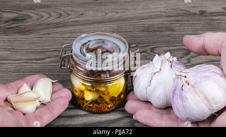 Vintage vasetto in vetro e le mani con garlics. Allium sativum. Una sana spicchi di aglio e decapati in olio, erbe, stagionatura a caldo. Verdure piccanti, sfondo legno. Foto Stock