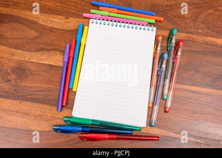 Rilegato a spirale rivestita notepad circondato da diverse penne colorate Foto Stock