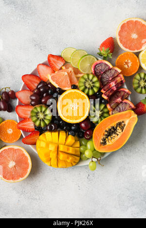 Materie frutti bacche platter, mango, arance e kiwi fragole, mirtilli pompelmo uva, mele sulla piastra bianca, su off tavolo bianco, top v Foto Stock