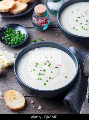 Il cavolfiore, crema di patate zuppa di cipolla verde in vaso nero su sfondo di legno Foto Stock