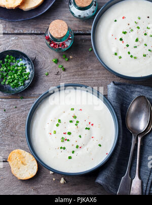 Il cavolfiore, crema di patate zuppa di cipolla verde in vaso nero su sfondo di legno. Vista superiore Foto Stock