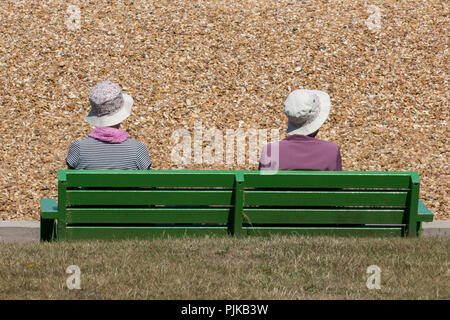 Due persone anziane o di un pensionato giovane seduto su un dipinto di verde una panchina nel parco in riva al mare a Cowes sull'isola di Wight. coppia in pensione a costa. Foto Stock