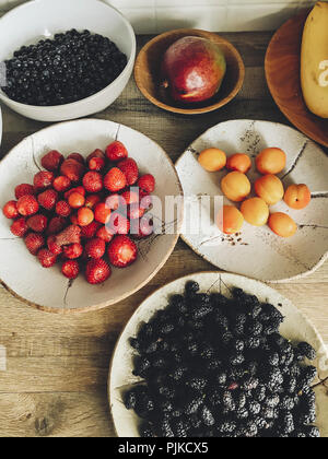 Estate fresca frutta in ceramica ciotole sul tavolo di legno in cucina. mirtilli, manghi, albicocche fragole e banane, gelso dal mercato. zero Foto Stock