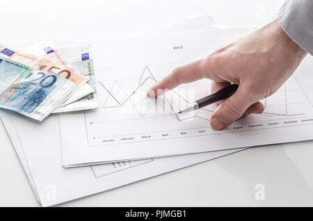 Vista ritagliata di un uomo rivolto alla relazione finanziaria con denaro euro su un tavolo. Foto Stock
