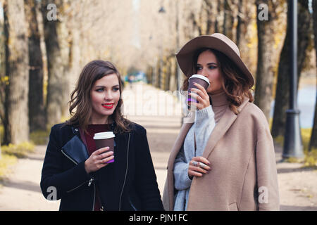 Felici donne di bere il caffè per andare all'aperto nel parco di autunno Foto Stock