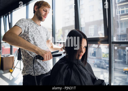 Bella donna felice mentre parrucchiere è la raddrizzatura i suoi capelli in salone. Nuovo taglio di capelli o Acconciatura per la giovane donna. Foto Stock