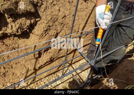 Lavoratori mani con filo di acciaio e di pinze per fissare rebar prima di calcestruzzo viene riversato su di esso 2018 Foto Stock