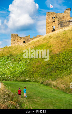 Tynemouth, Inghilterra - Agosto 2, 2018: due ragazzi con un calcio lo sguardo verso il Priorato di Tynemouth e Castello. Foto Stock