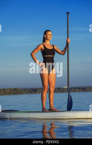 SUP fiducioso del costume da bagno donna in piedi con un dispositivo di compressione sulla tavola da surf Foto Stock