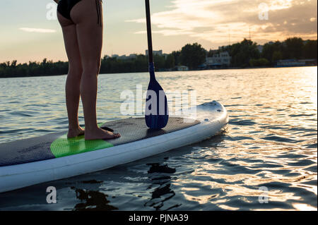 SUP fiducioso del costume da bagno donna in piedi con un dispositivo di compressione sulla tavola da surf, gambe Foto Stock