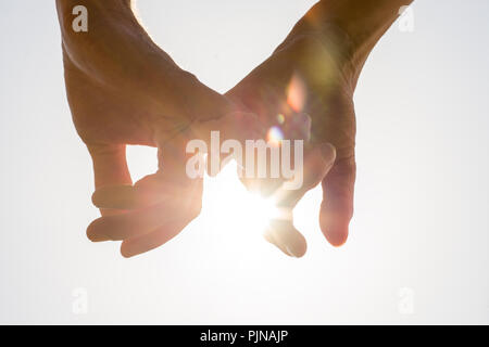 Giovane tenendo le mani verso il sole con sole luminoso flare tra il profilarsi le dita su un pallido cielo blu, vista ravvicinata in una immagine concettuale. Foto Stock