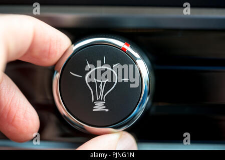 In prossimità delle dita di un uomo ruotando un pulsante con un disegnati a mano illuminata la lampadina di luce bianca su un pezzo di equipaggiamento elettronico concettuale del Foto Stock