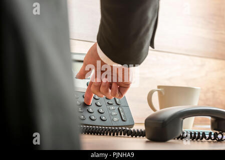 Imprenditore di comporre il numero di telefono su un classico nero telefono fisso con ricevitore sganciato e tazza di caffè sulla sua scrivania, angolo basso v Foto Stock